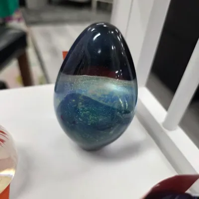 Sale Photo Thumbnail #109: Egg-shaped art glass paperweight featuring iridescent blue, green, and dark swirl patterns inside.