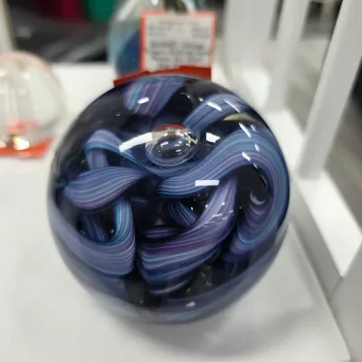 Sale Photo Thumbnail #110: Round art glass paperweight featuring swirl interior patterns in shades of blue and purple with an embedded controlled bubble.