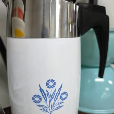 Sale Photo Thumbnail #179: Vintage Corning Ware electric coffee percolator featuring the iconic Cornflower Blue pattern, complete with stainless steel trim and a black composite handle.