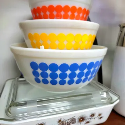 Sale Photo Thumbnail #180: Vintage Fire-King primary dots nesting bowl set stacked atop a Pyrex Pinecone covered casserole dish.