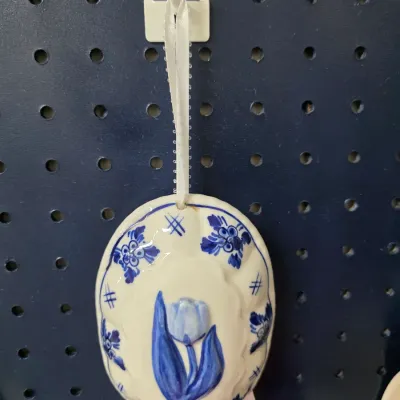 Sale Photo Thumbnail #202: Oval ceramic hanging mold featuring a Delft blue style tulip motif, complete with a white ribbon hanging strap.