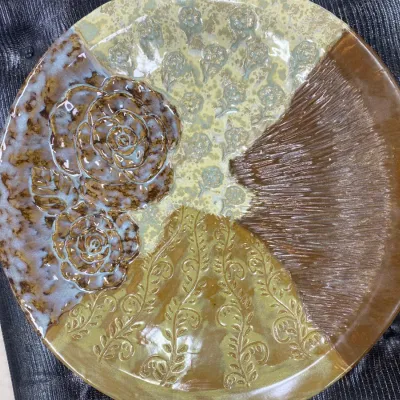 Sale Photo Thumbnail #329: Handcrafted studio pottery platter featuring a multi-patterned design in earth tones, complete with raised floral motifs and textured glazes.