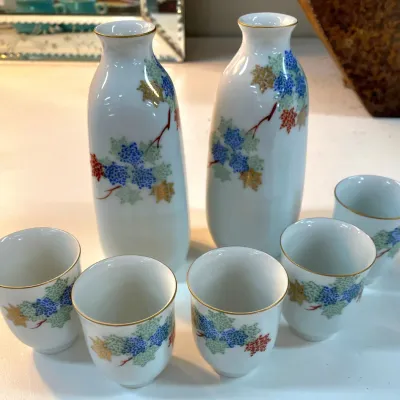 Sale Photo Thumbnail #347: Japanese porcelain sake set comprising two bottles and five matching cups, decorated with colorful maple leaf motifs and gold trim.