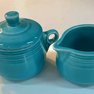 Sale Photo Thumbnail #348: Vintage turquoise Fiestaware sugar bowl with lid and matching creamer set, featuring ring-handled details and concentric line design.