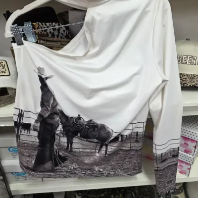 Sale Photo Thumbnail #358: White cut-out one-shoulder mock neck top featuring a photographic print of a cowboy and horse. Modern western style garment displayed on a hanger in good condition.