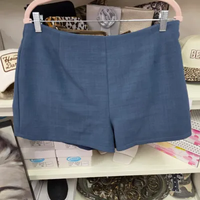 Sale Photo Thumbnail #368: Pair of women's dusty blue textured shorts displayed on a pink velvet hanger in a retail shelf setting.