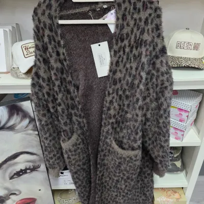 Sale Photo Thumbnail #375: Fuzzy leopard-print open-front cardigan sweater with retail tags intact, hanging in front of display shelves.