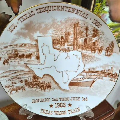 Sale Photo Thumbnail #381: 1986 Texas Sesquicentennial commemorative porcelain collector plate featuring Texas Wagon Train artwork and gold rim detail.