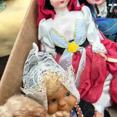 Sale Photo Thumbnail #385: Collection of vintage international folk souvenir dolls, featuring dressed figures in traditional European attire, including a Scottish bagpiper and a girl in a red bonnet.