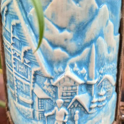 Sale Photo Thumbnail #398: Vintage molded ceramic beer stein detailing a relief scene of a skier in an Alpine village with mountains in the background.
