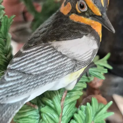 Sale Photo Thumbnail #399: Hand-painted porcelain bird figurine featuring intricate feather detailing and vibrant orange, black, and white plumage, perched on a faux pine branch.