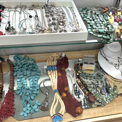 Sale Photo Thumbnail #406: Collection of vintage statement necklaces displayed on glass shelves, featuring turquoise, beaded, liquid silver, and natural stone designs.