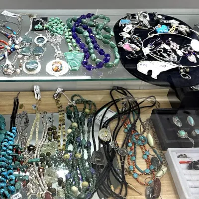 Sale Photo Thumbnail #407: Collection of Southwestern and Native American-style jewelry displayed in a glass case, featuring turquoise nugget necklaces, sterling silver pendants, beaded strands, bolo ties, and silver rings.
