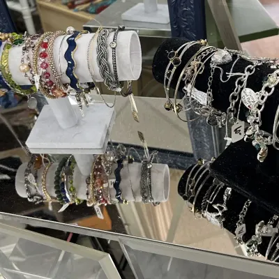 Sale Photo Thumbnail #413: Collection of assorted fashion bracelets, charm bangles, and beaded wristwear displayed on T-bar stands over a mirrored tabletop.