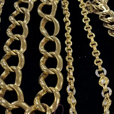 Sale Photo Thumbnail #414: Assortment of vintage gold-tone chain necklaces, western-style belt buckles, and a faux pearl bracelet arranged on black felt.