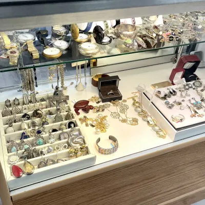 Sale Photo Thumbnail #416: Glass display case filled with vintage and contemporary jewelry, including sterling silver pendants, gold-tone chain necklaces, gemstone rings, cuff bracelets, and pocket watches.