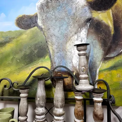 Sale Photo Thumbnail #443: A collection of turned wooden candle holders with a whitewashed finish, displayed in front of a textured oil painting of a cow.