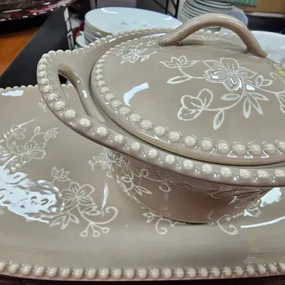 Sale Photo Thumbnail #477: Taupe ceramic serving set featuring a covered casserole dish resting on a matching oval platter, both decorated with beaded rims and etched white floral designs.