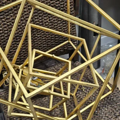 Sale Photo Thumbnail #488: Contemporary gold-toned geometric metal wire cage pendant light fixture resting on a woven wicker chair.