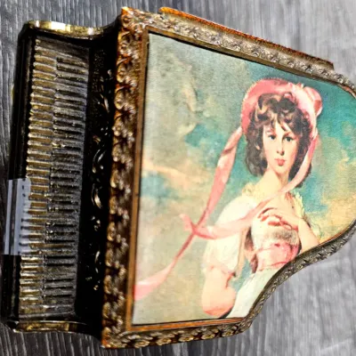 Sale Photo Thumbnail #496: Vintage grand piano-shaped music box featuring an ornate brass-tone case and a top inset portrait of Thomas Lawrence's 'Pinkie'.