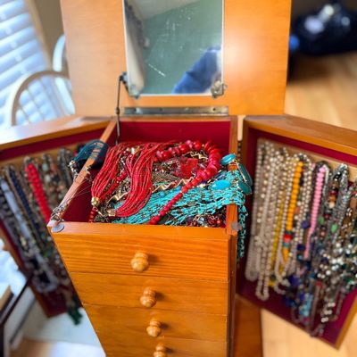 Sale Photo Thumbnail #9: Standing wooden jewelry armoire filled with assorted costume jewelry, featuring a flip-top mirror, drawers, and side necklace doors.