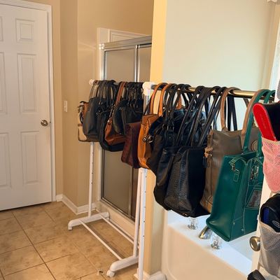 Sale Photo Thumbnail #27: Collection of women's leather and synthetic handbags in various colors hanging on two white rolling clothing racks.