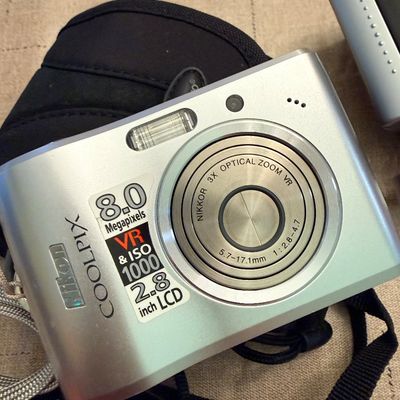 Sale Photo Thumbnail #32: Silver Nikon Coolpix 8.0 megapixel digital point-and-shoot camera with a 3x Nikkor optical zoom VR lens, wrist strap, and black padded case.
