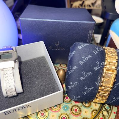 Sale Photo Thumbnail #41: Two Bulova watches, including a gold-tone dress watch on a branded display cushion and a vintage silver-tone digital watch in its original box.