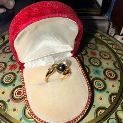 Sale Photo Thumbnail #43: Gold ring featuring a black pearl and a white pearl bypass setting, presented in a vintage red velvet clam-shell display box.