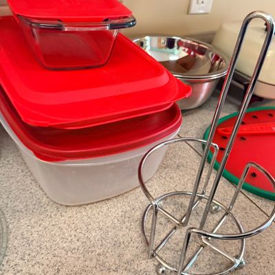 Sale Photo Thumbnail #57: Selection of kitchen wares including a metal wire paper towel holder, Pyrex and plastic food storage containers with red lids, and a stainless steel mixing bowl.