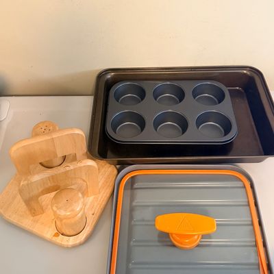Sale Photo Thumbnail #64: Collection of kitchen items including a wooden napkin holder and salt/pepper shaker set, a metal 6-cup muffin tin inside a baking pan, and a lid with an orange handle.