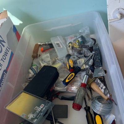 Sale Photo Thumbnail #103: Plastic storage bin filled with an assortment of hand tools and hardware, including screwdrivers, utility knives, and a roll of wire.
