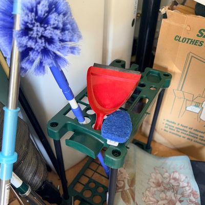 Sale Photo Thumbnail #109: Assorted cleaning tools, including a purple cobweb duster, red dustpan, and scrubbing pad, resting on a green plastic tool organizer stand.