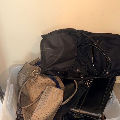 Sale Photo Thumbnail #137: A clear plastic storage bin filled with various women's handbags, including a taupe ostrich-embossed tote, a black nylon bag, and a black leather shoulder bag.