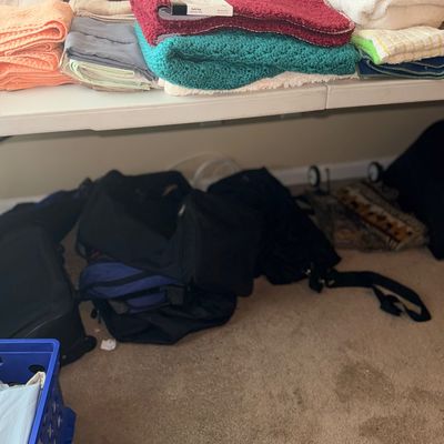 Sale Photo Thumbnail #139: Assorted folded bath towels and linens arranged on a white folding table, with duffel bags and luggage stored underneath on the carpet.