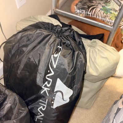 Sale Photo Thumbnail #148: Black Ozark Trail drawstring storage bag containing outdoor or camping gear, accompanied by additional beige duffel bags.