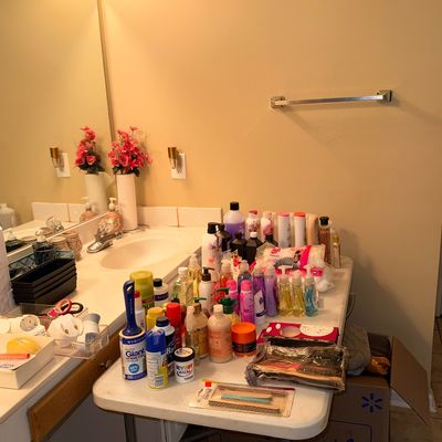 Sale Photo Thumbnail #171: Large assortment of toiletries, personal care products, lotions, and cleaning supplies arranged on a folding table and bathroom counter.