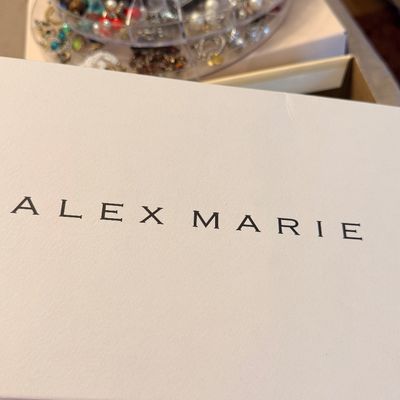 Sale Photo Thumbnail #227: White Alex Marie shoebox positioned in front of a multi-tiered clear plastic jewelry organizer filled with various costume jewelry pieces.