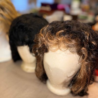 Sale Photo Thumbnail #251: Collection of styled wigs displayed on mannequin heads, featuring short curly brown and black synthetic or human hair options.