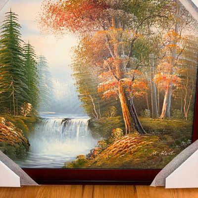 Sale Photo Thumbnail #265: Framed landscape oil painting depicting a waterfall in an autumn forest, signed by the artist M. Scott, with protective foam corners on the dark wood frame.
