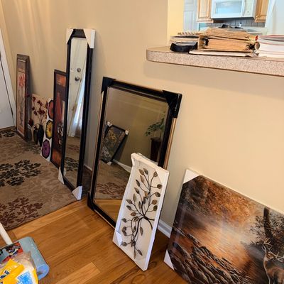 Sale Photo Thumbnail #268: Selection of home decor including framed mirrors, floral art prints, metal wall sculpture, and a wildlife canvas print lined up against a hallway wall.