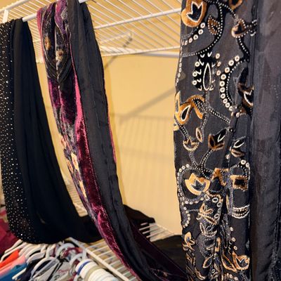Sale Photo Thumbnail #307: Assorted fashion scarves, including a black sheer scarf with gold and silver embroidery and a purple velvet patterned scarf, hanging on a wire closet shelf.