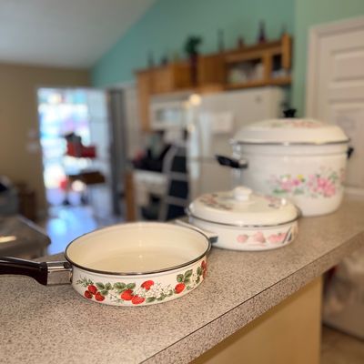 Sale Photo Thumbnail #316: Vintage enamelware cookware set featuring a strawberry pattern skillet and floral-patterned lidded pots, circa 1970s or 1980s.
