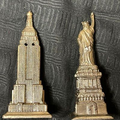 Vintage metal souvenir salt and pepper shakers shaped like the Empire State Building and the Statue of Liberty, showing a weathered...