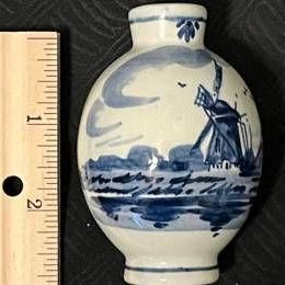Small Delft blue and white ceramic vase featuring a hand-painted windmill scene, shown next to a wooden ruler for scale.