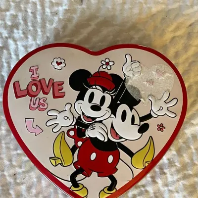 Heart-shaped Disney tin featuring Mickey and Minnie Mouse with "I Love Us" text, showing some sticker residue on the front.