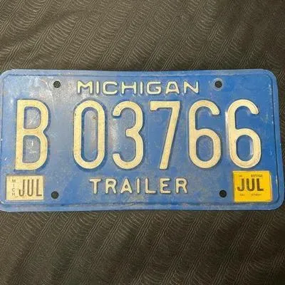 Vintage blue Michigan trailer license plate with white embossed lettering, featuring a July registration sticker.