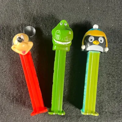 Trio of vintage Pez dispensers featuring Mickey Mouse, Rex from Toy Story, and a penguin character, showing light wear from age.
