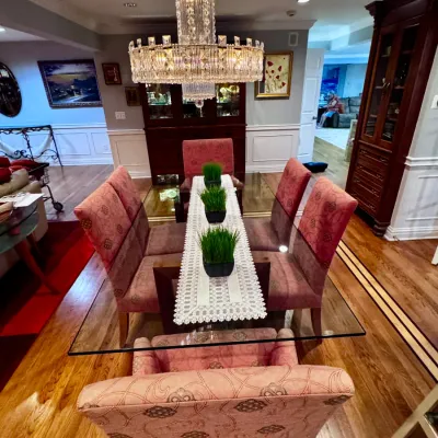 Sale Photo Thumbnail #2: Glass-top dining room table paired with pink patterned upholstered chairs, set beneath a multi-tiered crystal chandelier.