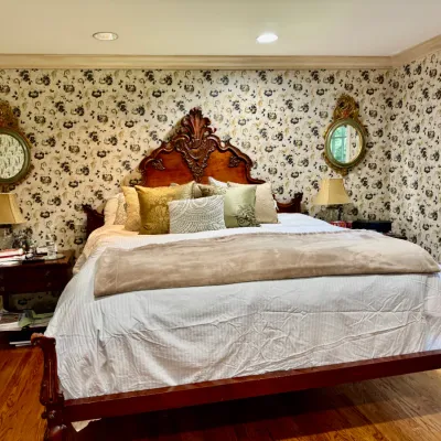 Sale Photo Thumbnail #9: Ornate Victorian-style carved wood king bed frame, flanked by matching nightstands, lamps, and decorative oval mirrors.